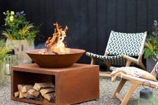 a simple and stylish outdoor fire pit space with light-stained chairs, a metal bow and a fire bowl on top plus potted blooms