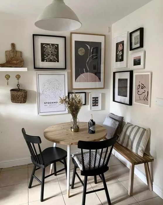 a small and cool dining space with a floating bench, a stained table, black chairs and a catchy corner gallery wall plus a pendant lamp