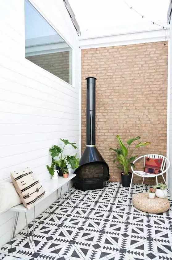 a small inner patio with black and white tiles, a white bench and a chair, potted plants, a jute pouf and a black Malm fireplace