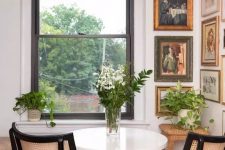 a small vintage dining space with a beautiful vintage corner gallery wall, a white table, neutral chairs, greenery and blooms and a stylish chandelier