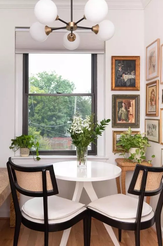 a small vintage dining space with a beautiful vintage corner gallery wall, a white table, neutral chairs, greenery and blooms and a stylish chandelier