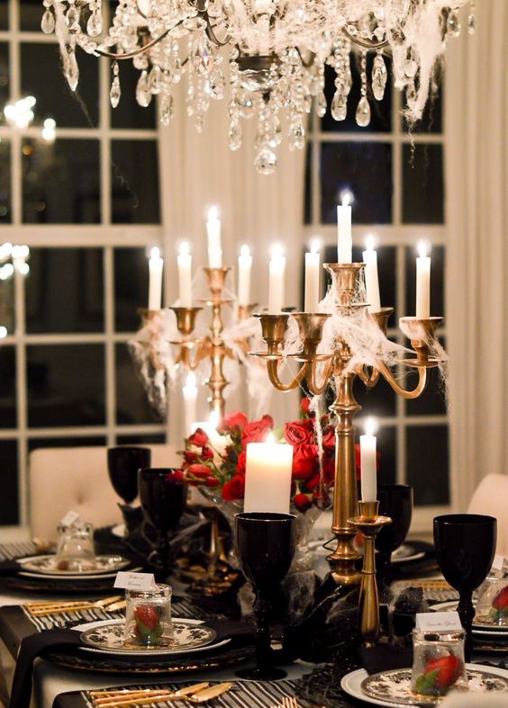 a sophisticated Halloween tablescape with black chargers and glasses, gold spiderweb candelabras, red roses and gold cutlery