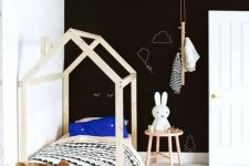 a stylish Scandinavian kid’s room with a black accent wall, a wooden house-shaped bed, graphic bedding, a wooden a side table with a Miffy lamp and a basket for storage