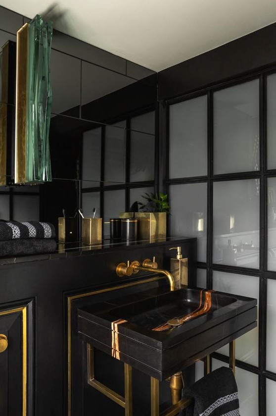 a stylish and luxurious powder room in black and gold, with gold framing and accessories plus a chic marble sink