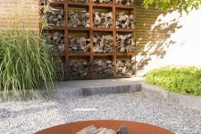 a stylish and neat garden with greenery, a firewood storage wall and a fire bowl on the gravel is a lovely space