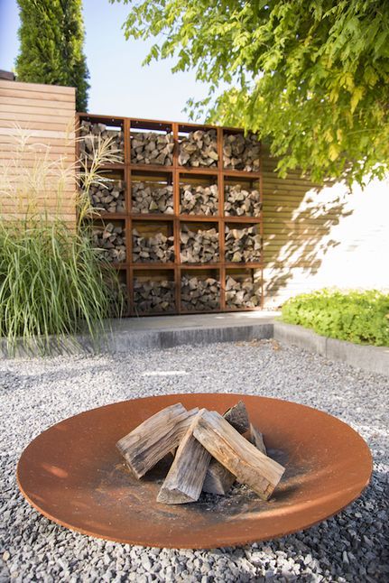 a stylish and neat garden with greenery, a firewood storage wall and a fire bowl on the gravel is a lovely space