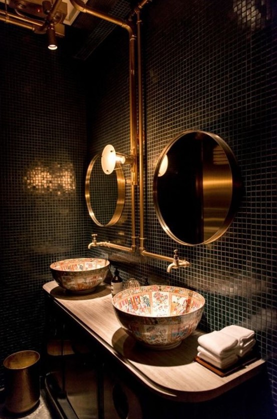 a stylish bathroom with black tiles, gold mirrors, painted sinks and exposed gold pipes is jaw dropping