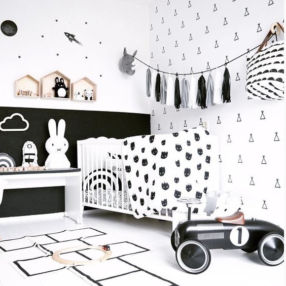 a stylish black and white nursery with monochromatic furniture, a tassel garland, a white crib and lots of prints
