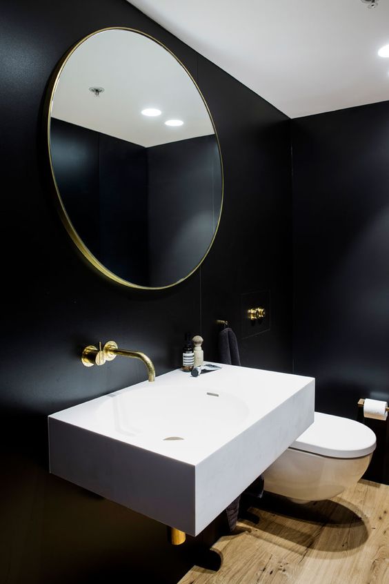 a stylish contemporary powder room with black walls, a laminate floor, a wall-mounted sink and gold touches for more chic