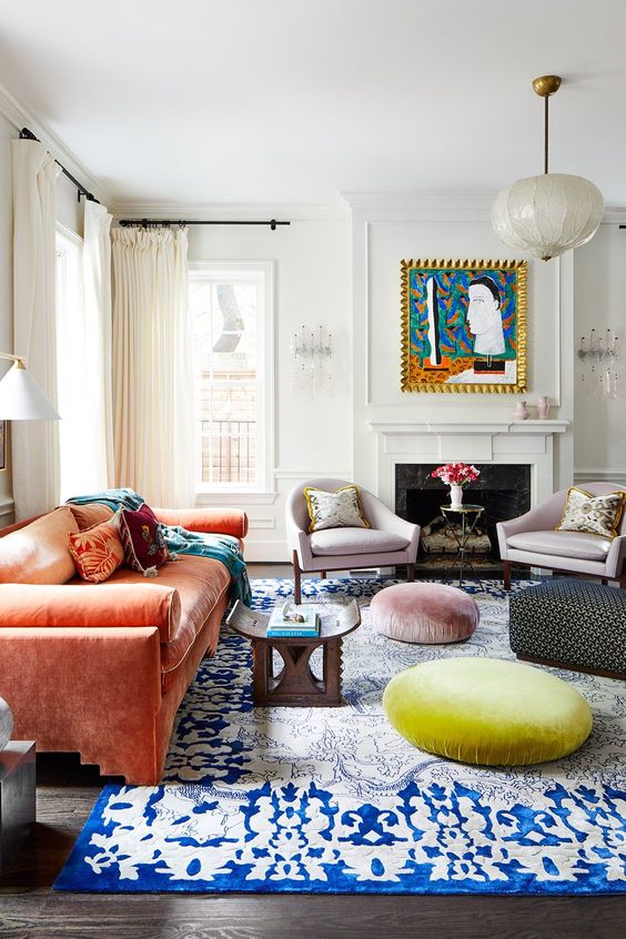 a stylish eclectic living room with a fireplace, an orange sofa, pastel cushions and chairs, a printed rug and a bold artwork