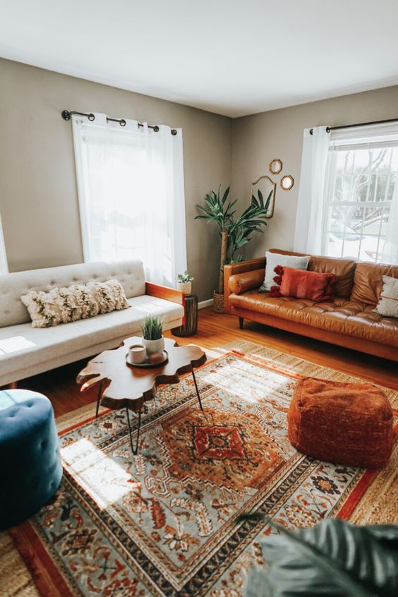 a stylish eclectic living room with grey walls, a white sofa, an amber leather sofa, a bold printed rug, a living edge coffee table