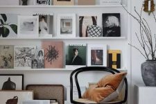 a stylish gallery wall with multiple white ledges, various magazines, books and artworks plus a lamp that accents it