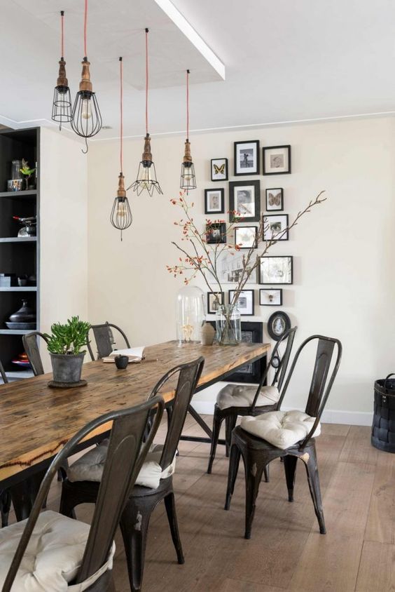 a stylish industrial dining room with a wooden table, metal chairs with cushions, industrial pendant bulbs and a gallery wall