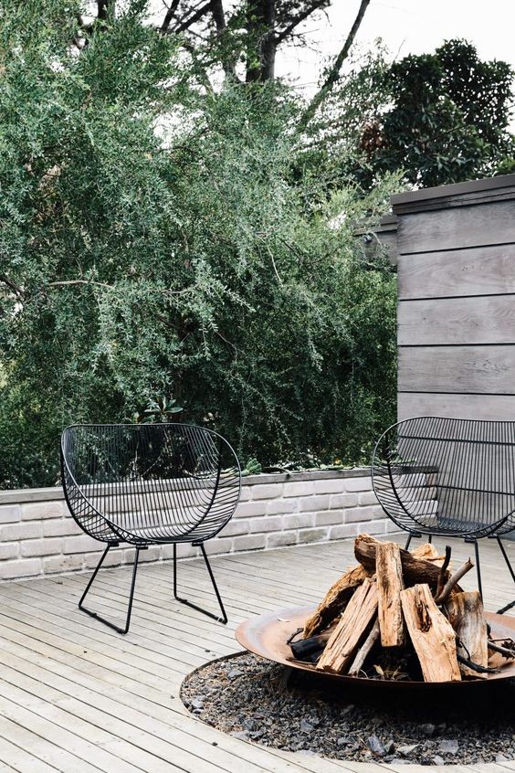 a stylish modern deck done with whitewashed wood, elegant black metal chairs, a metal fire bowl is impeccable