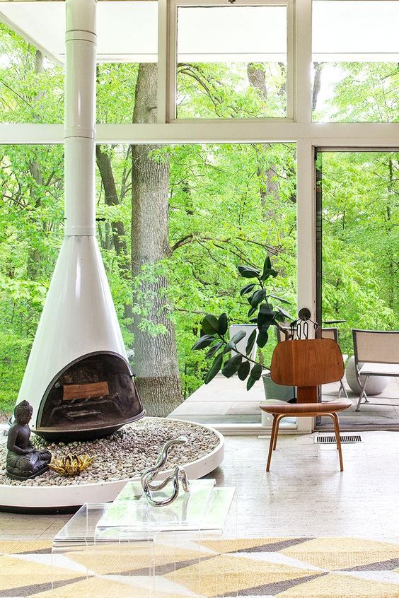 a stylish neutral living room with a white Malm fireplace, a plywood chair and glazed walls to enjoy forest views