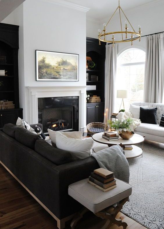 a traditional black and white living room with built in shelves, a fireplace, a black and white sofa, a round tiered table and a round chandelier
