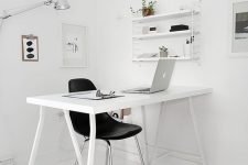 a very minimal Nordic home office with a white desk, a black chair, some stools and a wall-mounted shelf plus lamps