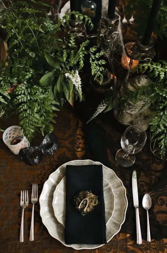 a vintage Halloween table setting with black and white touches, greenery, black candles in vintage candleholders, spiderwebs and hay is a creative idea