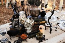 a vintage Halloween table setting with spiders, a silver skull, black blooms, vintage cameras and printed plates
