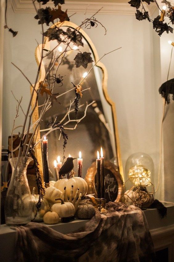 a vintage console with pumpkins, blackbirds, witches' hands, black candles, branches with spiders and a vintage mirror