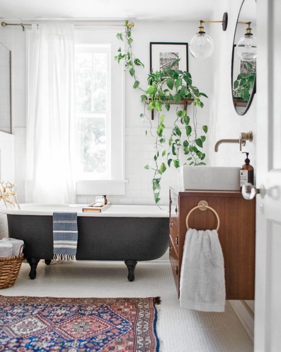 a vintage eclectic bathroom with a boho rug, a vintage black bathtub, potted greenery and a floatign vanity with a sink