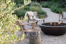 a welcoming and chic outdoor space with gravel on the ground, stained woven chairs, a large stone fire bowl and some neutral upholstery