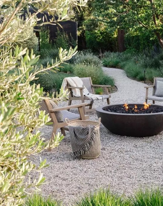 a welcoming and chic outdoor space with gravel on the ground, stained woven chairs, a large stone fire bowl and some neutral upholstery