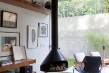 a welcoming mid-century modern living room with a black suspended Malm fireplace, a black leather chair, open shelves with books and art