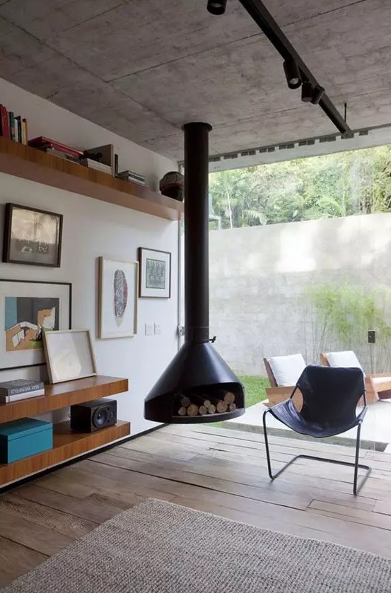 a welcoming mid century modern living room with a black suspended Malm fireplace, a black leather chair, open shelves with books and art