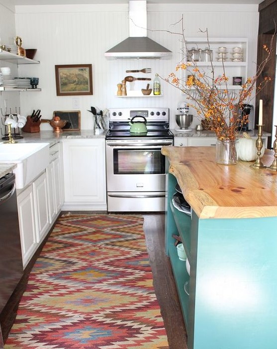 a white traditional kitchen, a colorful boho rug, a blue kitchen island with a wooden countertop with a living edge