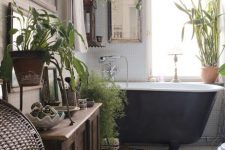 an eclectic bathroom with small scale tiles, a black clawfoot tiles, a stained cabinet, potted greenery, a mirror in a frame and a printed rug