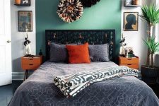 an eclectic bedroom with a green curved accent, a black bed with grey bedding, bold orange decor touches and nightstands, artwork, potted greenery and large pompoms