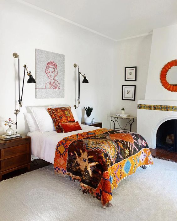 an eclectic bedroom with a vintage hearth with tiles, a bed with colorful bedding, dark stained nightstands, black sconces and potted plants