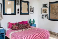 an eclectic bedroom with a wallpaper ceiling, a boho rug and bedding with pompoms, a variety of artworks and retro nightstands