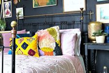 an eclectic bedroom with black walls, a forged bed with colorful bedding, black nightstands, potted plants, a gallery wall and layered rugs
