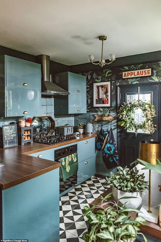 an eclectic kitchen with black walls, blue sleek cabinets, butcherblock countertops, a black and white tile floor and potted plants