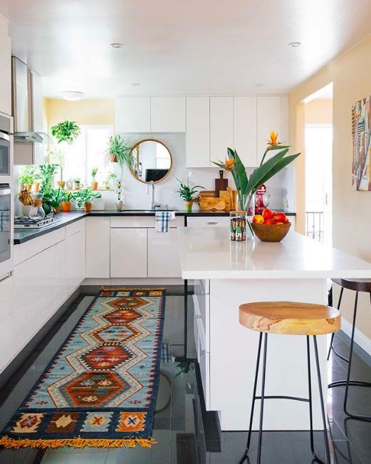 an eclectic kitchen with sleek white cabinets, black stone countertops, a bold rug, potted plants and stools