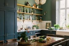 an eclectic kitchen with teal cabinets, green walls, white subway tiles, a crystal chandelier, a dark-stained table and benches and chairs