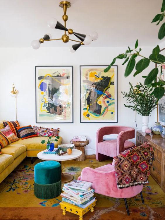 an eclectic living room with a yellow sofa and bright pillows, a bold printed rug, pink chairs, a colorful mini gallery wall and a stack of books