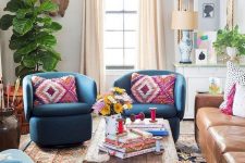an eclectic space with folksy and boho textiles, a mid-century modern chandelier, a leather sofa and bright blue chairs
