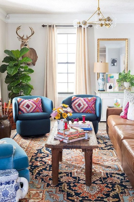 an eclectic space with folksy and boho textiles, a mid century modern chandelier, a leather sofa and bright blue chairs