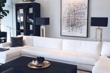 an edgy black and white living room with a white sectional, a black coffee table and chairs, a black bookcase and a floor lamp, a bold chandelier