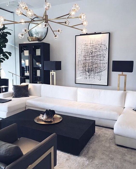 an edgy black and white living room with a white sectional, a black coffee table and chairs, a black bookcase and a floor lamp, a bold chandelier