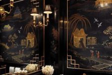 an exquisite black and gold bathroom with artwork, a gold ceiling, chic lamps, a black vanity and a gold sink