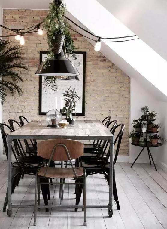 an industrial Scandinavian dining room with a brick accent wall, a metal and wood table, metal chairs, black pendant lamps and greenery