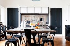 an industrial dining nook with a large table with a rough wooden tabletop, black metal chairs, a black pendant lamp