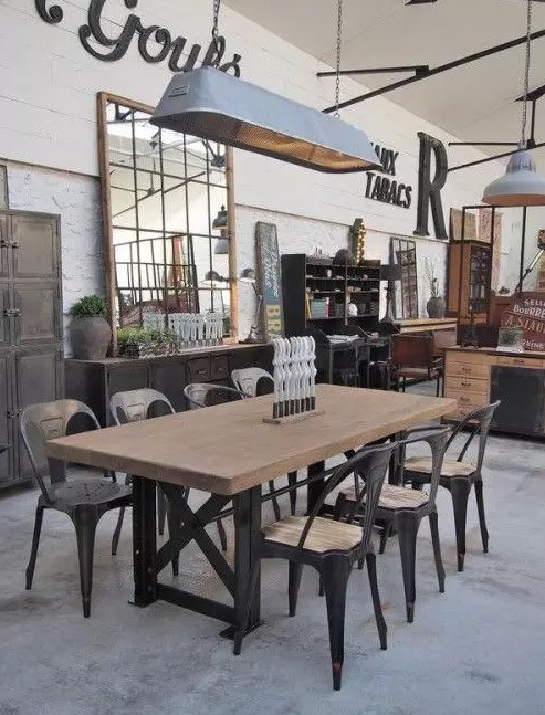 an industrial dining room with a large dining table on metal legs, matching chairs, a large metal pendant lamp and a metal credenza