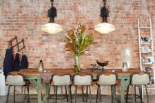 an industrial dining room with brick walls, an industrial dining table, tall metal stools, large pendant lamps on unique chains