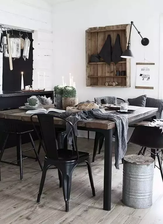 an industrial dining space with a black credenza, a minimal wood and metal table, black metal chairs and a black sconce