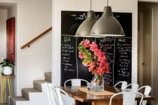 an industrial dining space with a large chalkboard, a stained table, white metal chairs and metal pendant lamps is a lovely space to have meals